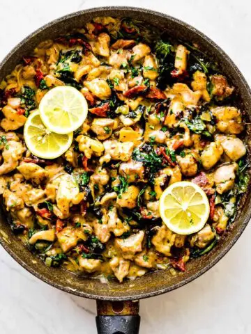 creamy garlic chicken in a pan with lemons sliced on top