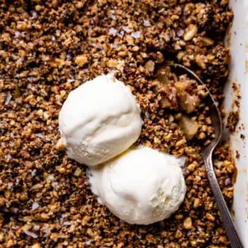 paleo apple crisp in a white casserole dish with vanilla ice cream scoops on top