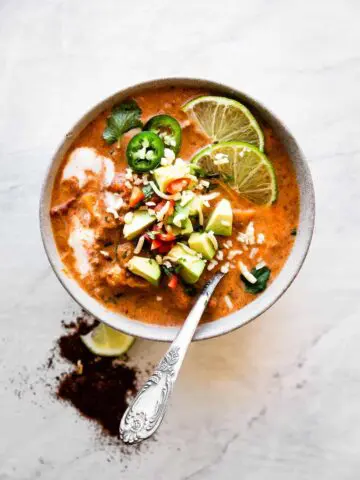 bowl of creamy taco soup with a spoon inside and avocado and limes on top