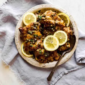 creamy chicken piccata on a ceramic plate with lemons on top