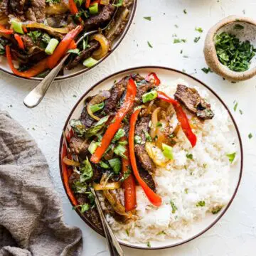 Thai basil beef on plates with green onions, cilantro, and rice