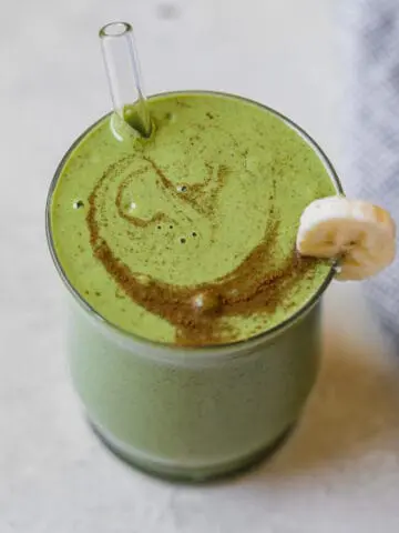 banana spinach smoothie in a cup with a glass straw