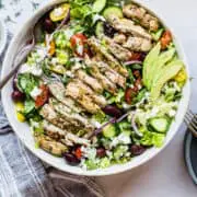 Greek chicken salad in a large bowl with a metal spoon