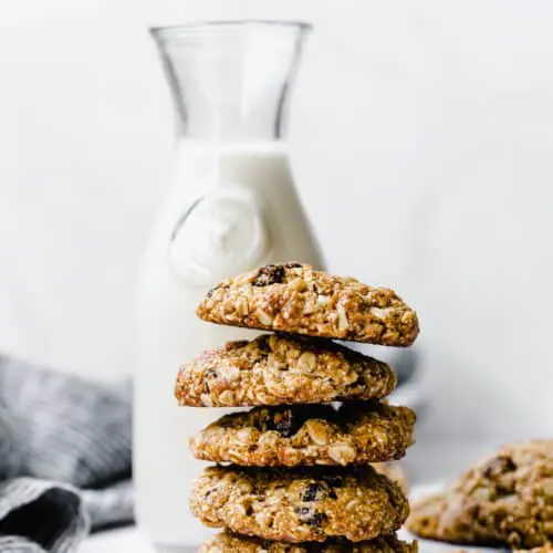 a stack of oatmeal raisin cookies with a jug of milk in the background
