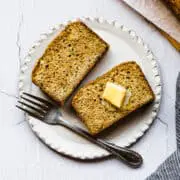two slices of zucchini bread on a a white plate with butter on top and a fork