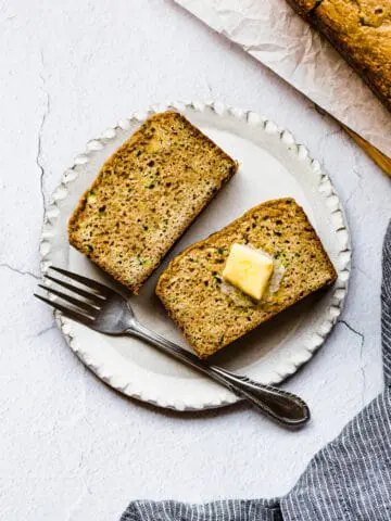 two slices of zucchini bread on a a white plate with butter on top and a fork