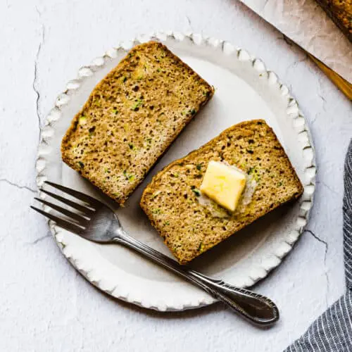 two slices of zucchini bread on a a white plate with butter on top and a fork
