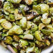 honey mustard brussels sprouts in a white ceramic bowl with a spoon inside