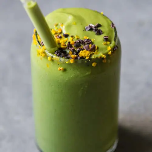 green avocado smoothie with a glass straw and bee pollen on top