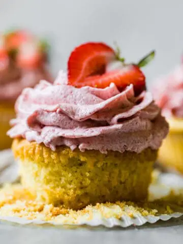 an unwrapped vanilla and strawberry cupcake with a fresh strawberry on top
