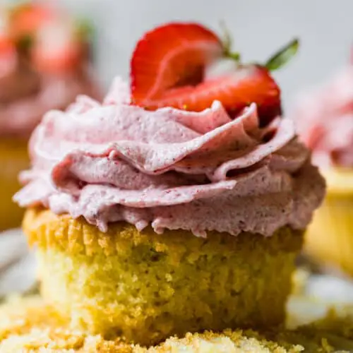 an unwrapped vanilla and strawberry cupcake with a fresh strawberry on top