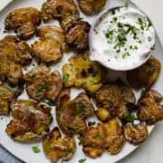 smashed potatoes on a plate with a creamy white dipping sauce on the side