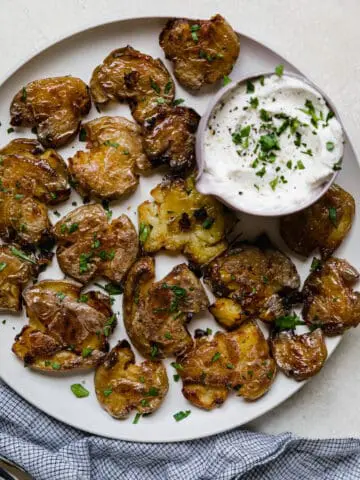 smashed potatoes on a plate with a creamy white dipping sauce on the side