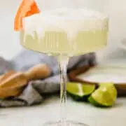 a frothy paloma in a coupe glass with a grapefruit wedge