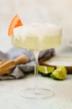 a frothy paloma in a coupe glass with a grapefruit wedge
