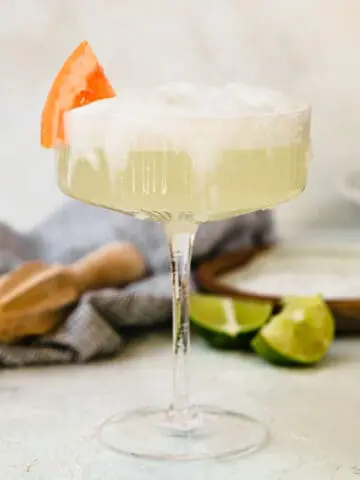 a frothy paloma in a coupe glass with a grapefruit wedge