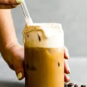 stirring irish cream coffee in a glass cup with a glass straw