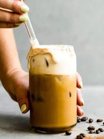 stirring irish cream coffee in a glass cup with a glass straw