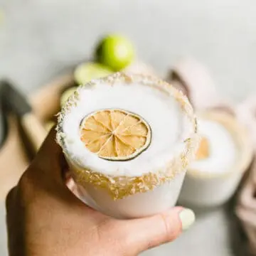 hand holding a frozen coconut margarita with a dehydrated lime on top