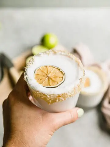 hand holding a frozen coconut margarita with a dehydrated lime on top