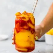 holding a frozen mangonada with a glass straw