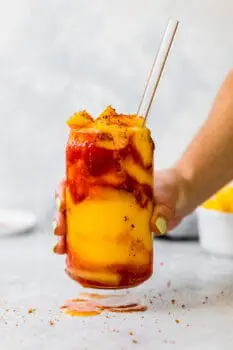 holding a frozen mangonada with a glass straw