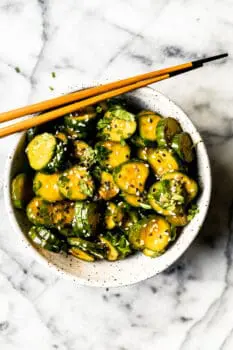 Korean cucumber salad in a ceramic bowl with sesame seeds and wooden chopsticks