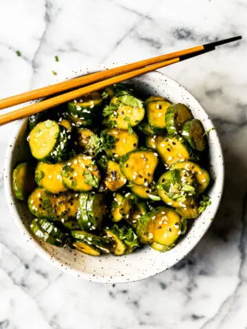 Korean cucumber salad in a ceramic bowl with sesame seeds and wooden chopsticks