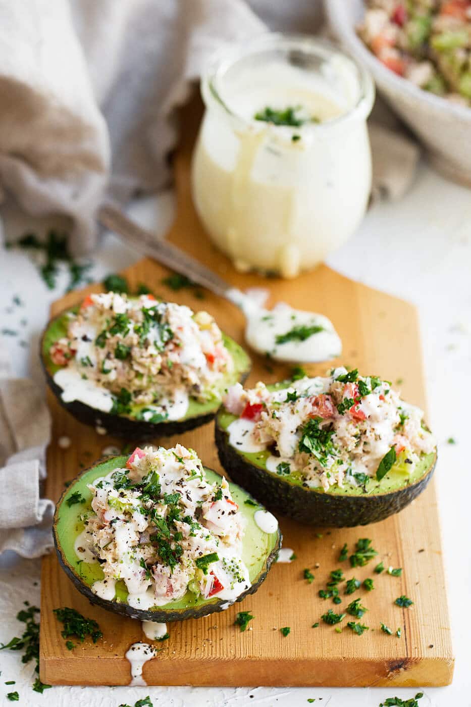 Avocados filled with tuna salad on a wooden chopping board with a spoon of paleo mayo