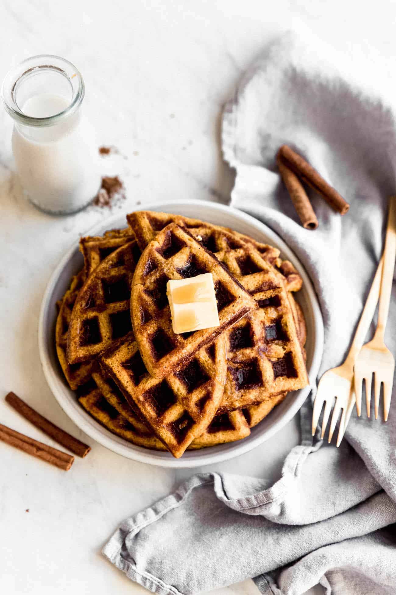 pumpkin waffles cut on a plate with butter on top and forks on the side