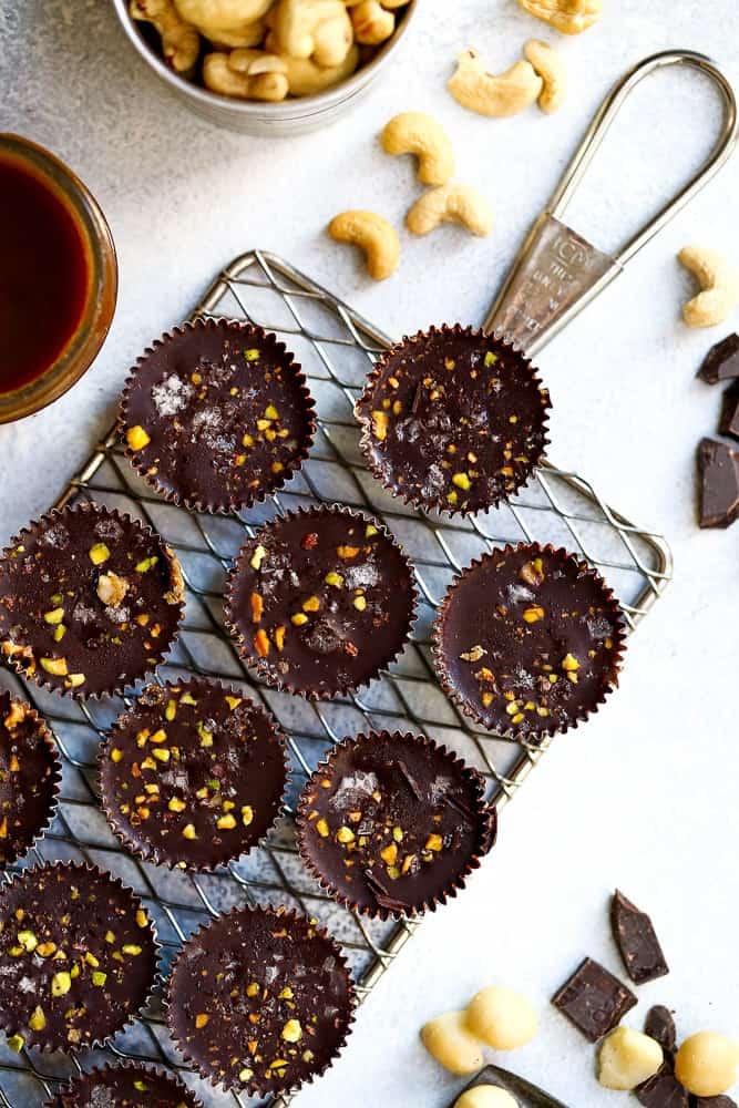 dark chocolate caramel cups on a stainless steel cooling rack with nuts on the side