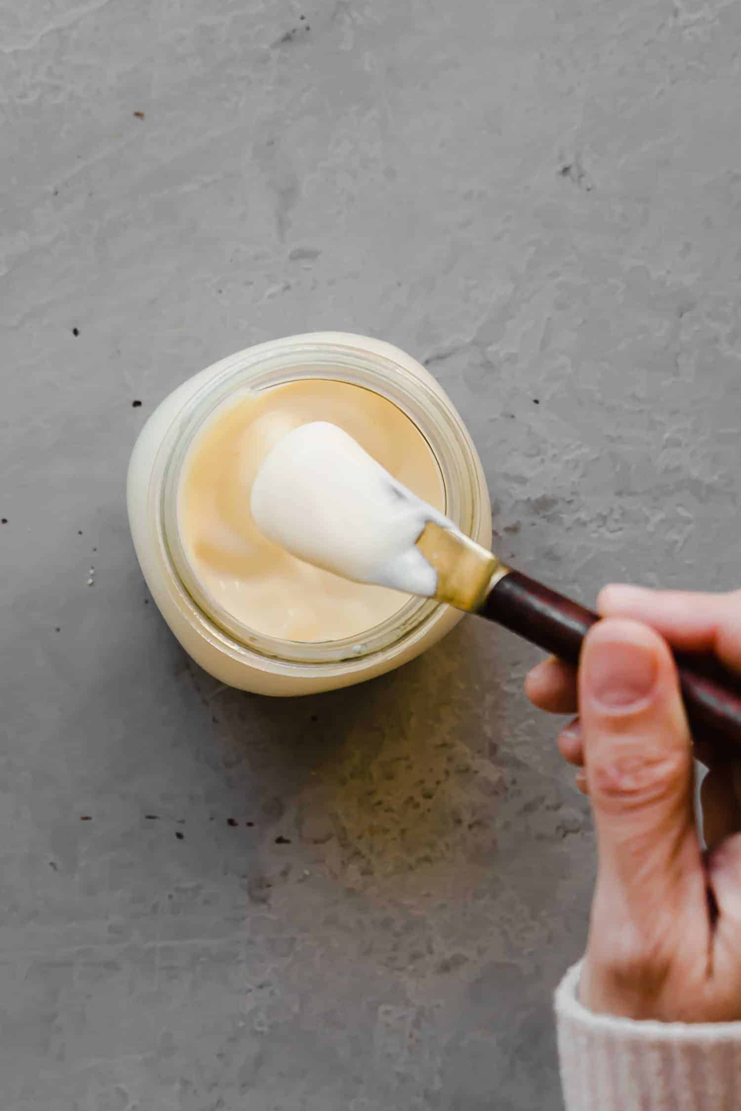 scooping homemade mayo out of a glass jar