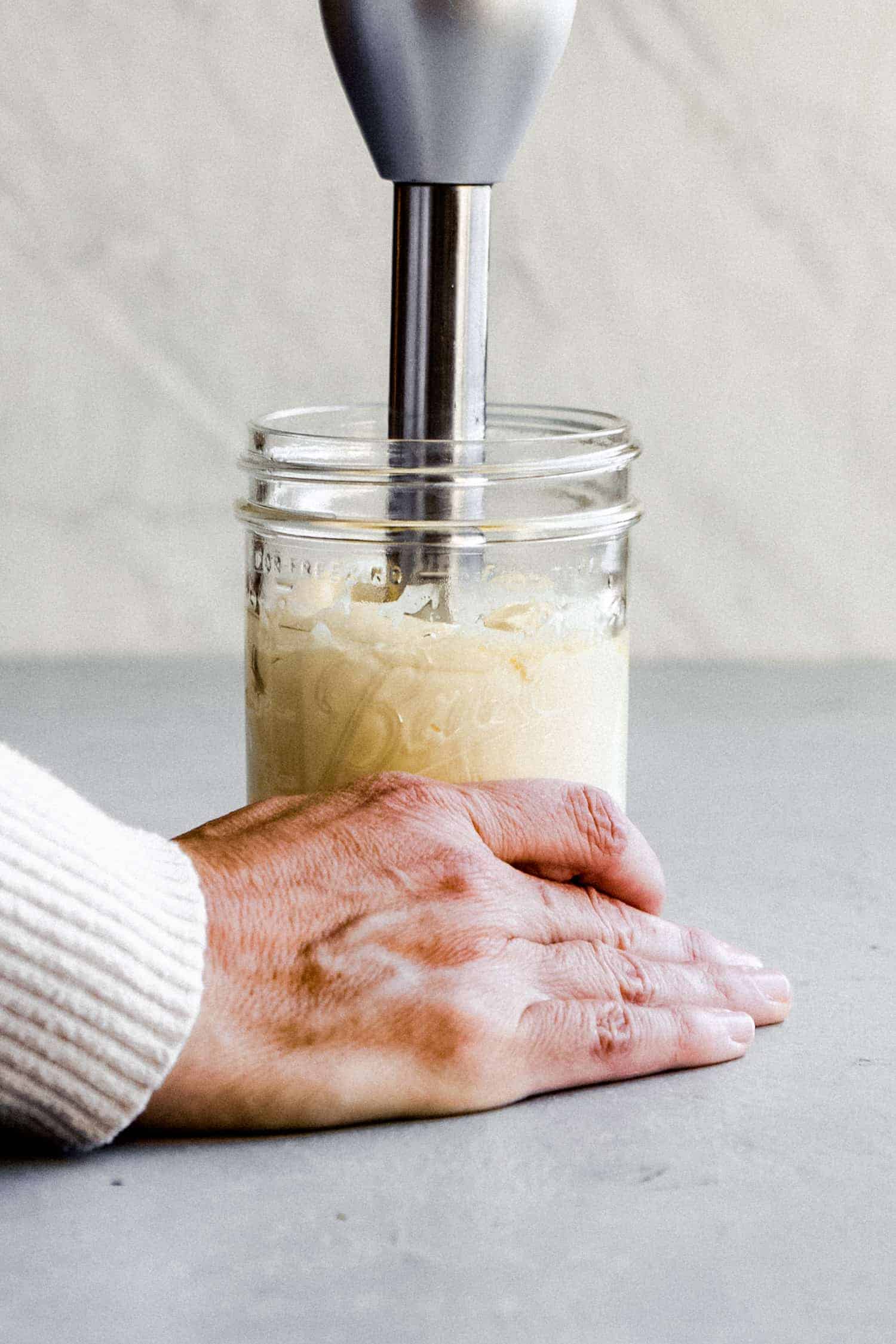 a hand holding the bottom of a glass jar while making homemade mayo