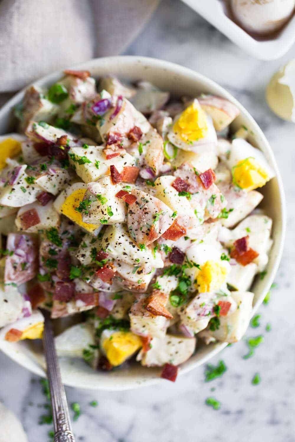 potato salad in a white bowl and fresh herbs with a spoon