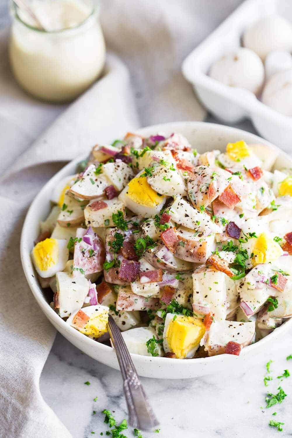 potato salad in a white bowl garnished with fresh herbs