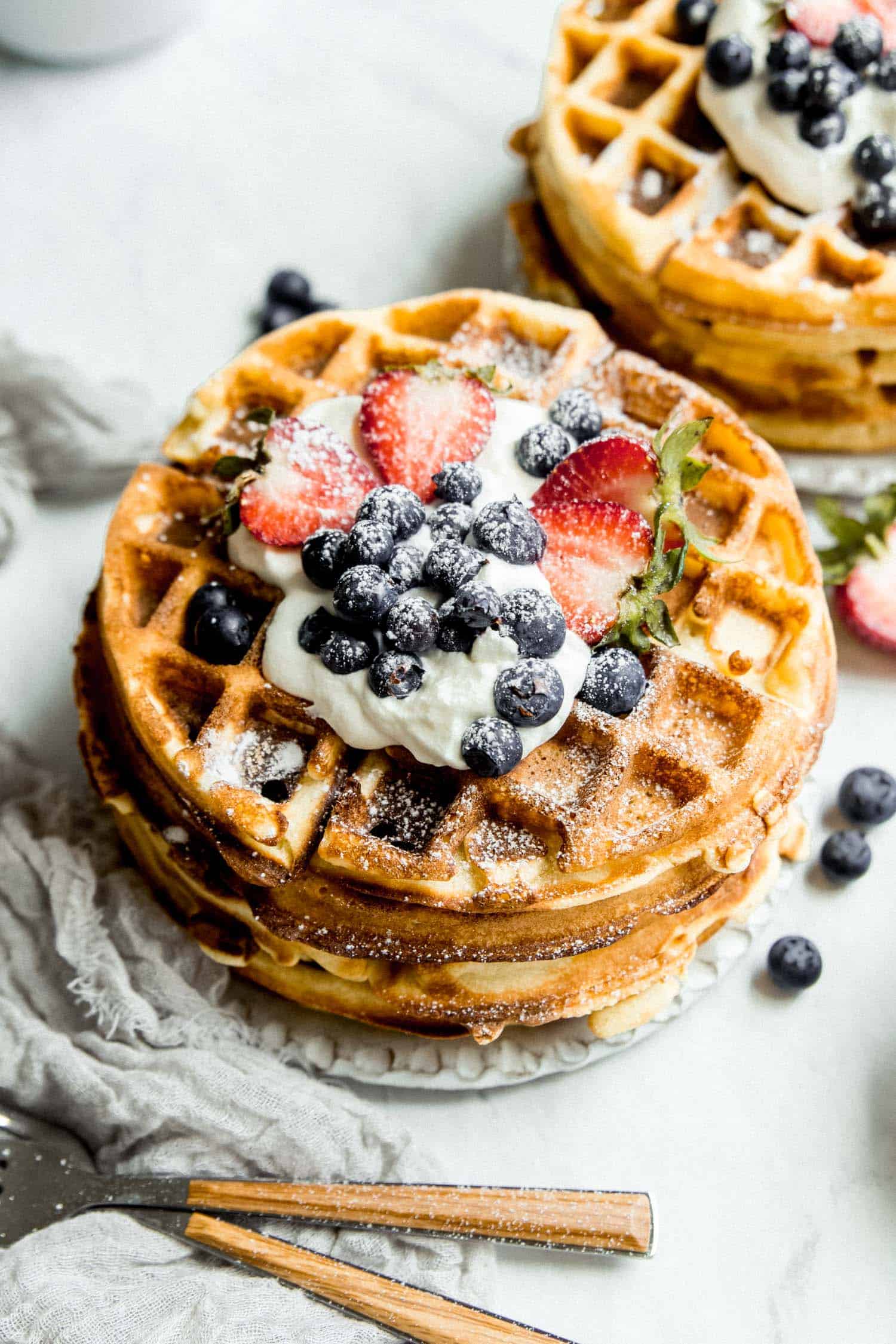 a stack of paleo waffles with berries and powdered sugar on top