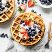 stack of waffles on a plate with berries and forks on the side