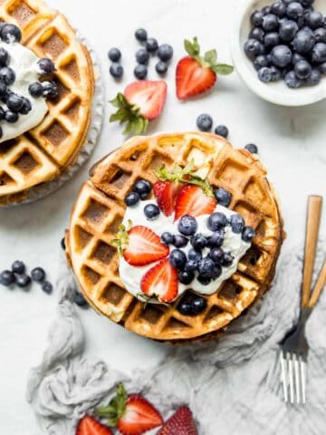 stack of waffles on a plate with berries and forks on the side