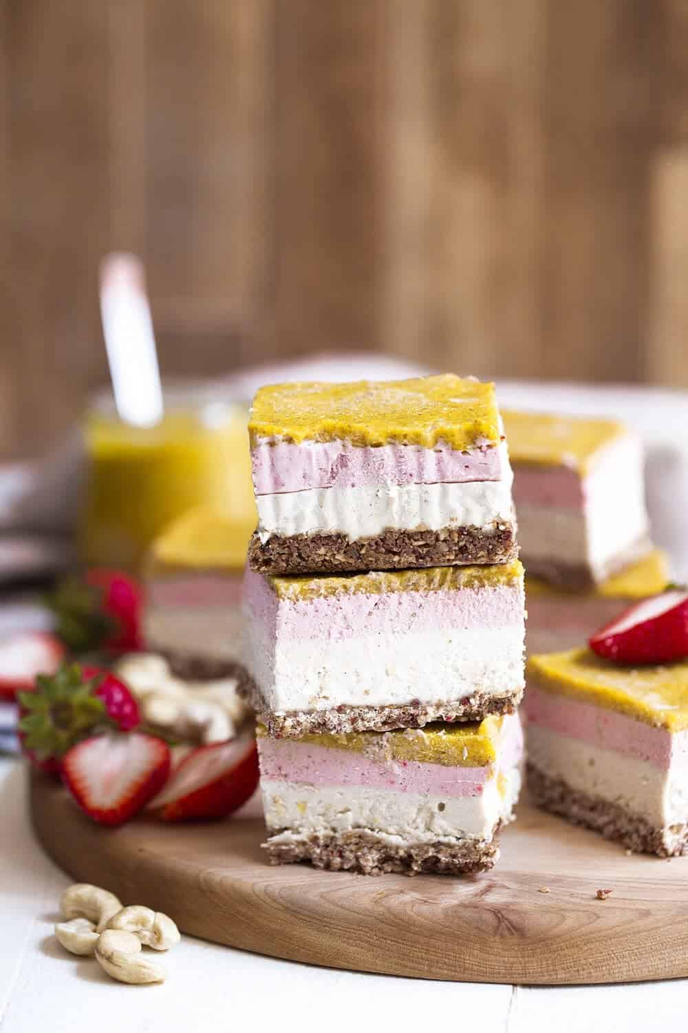 Strawberry & mango cheesecake bars with a granola crust cut into equal portions on a wooden board