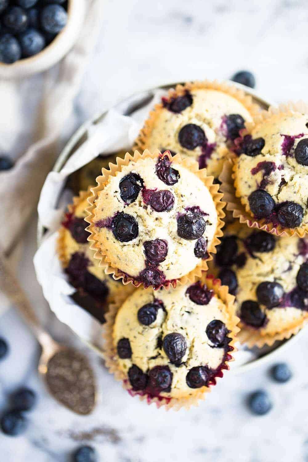 Gluten Free Vegan Blueberry Muffins stacked on top of each other in a serving dish with blueberries