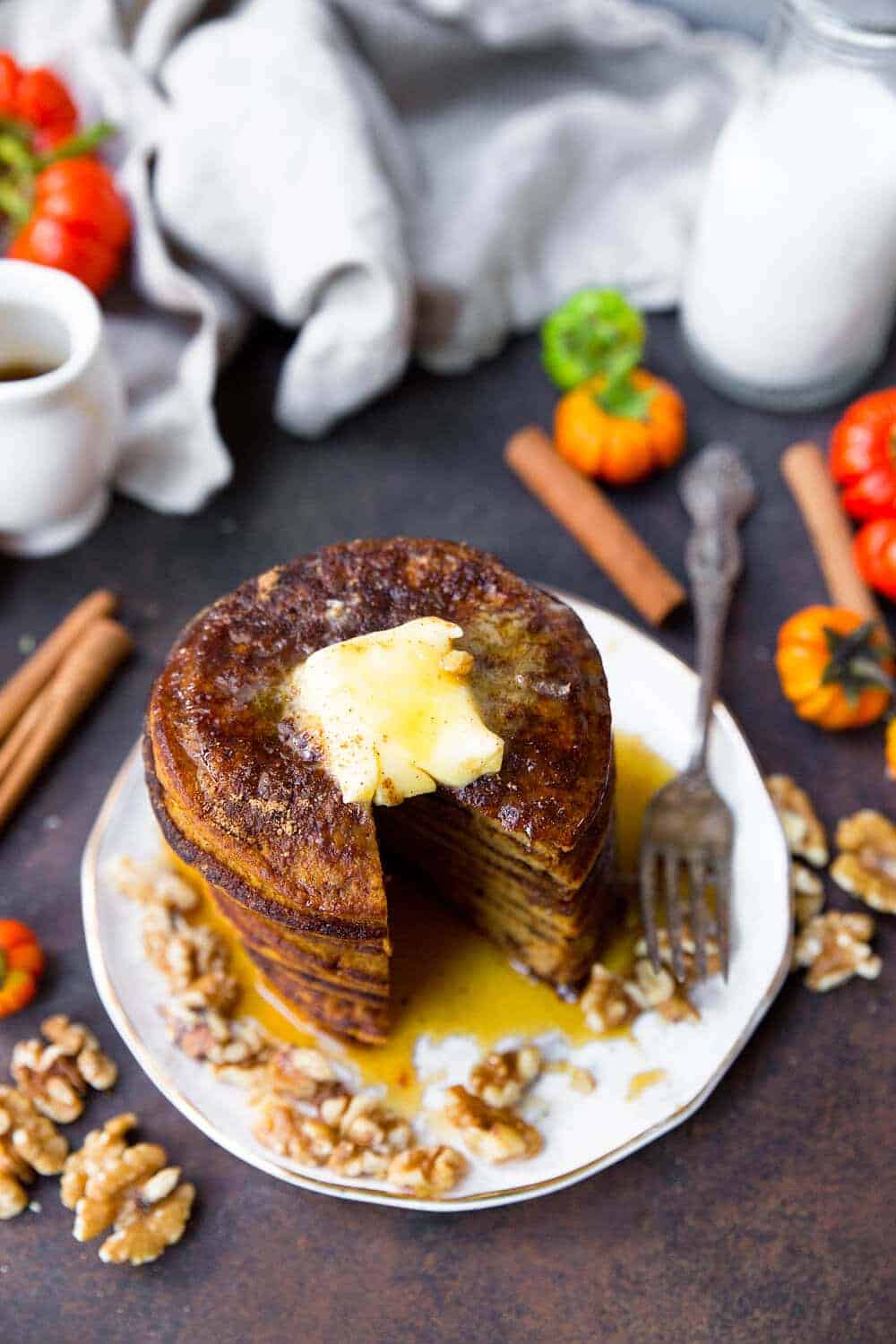 Coconut Flour Pumpkin Pancakes stacked on a white plate with butter and maple syrup