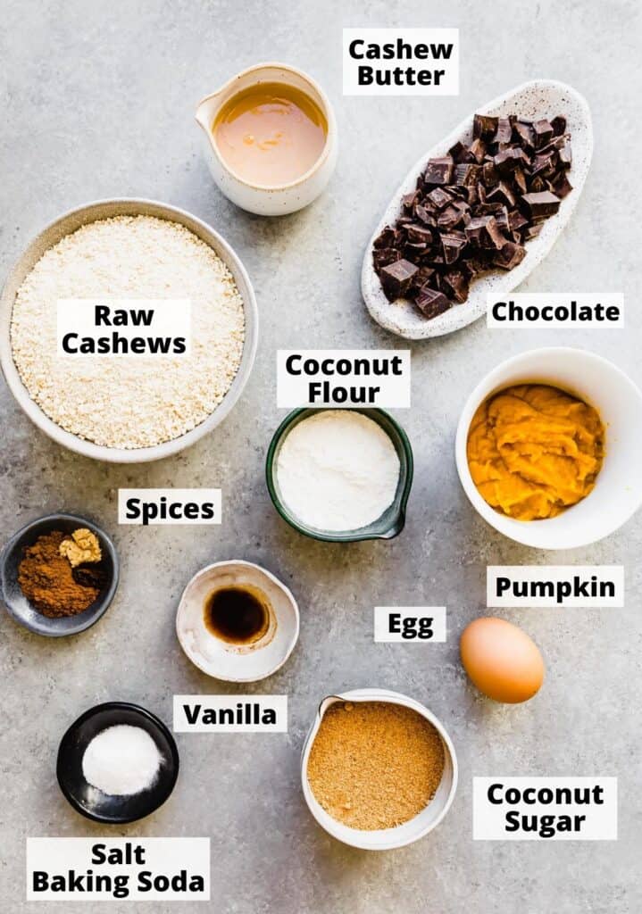 ingredients prepped to make pumpkin chocolate chip cookies: cashew butter, raw cashews, coconut flour, chocolate, spices, pumpkin, egg, vanilla, coconut sugar, salt baking soda