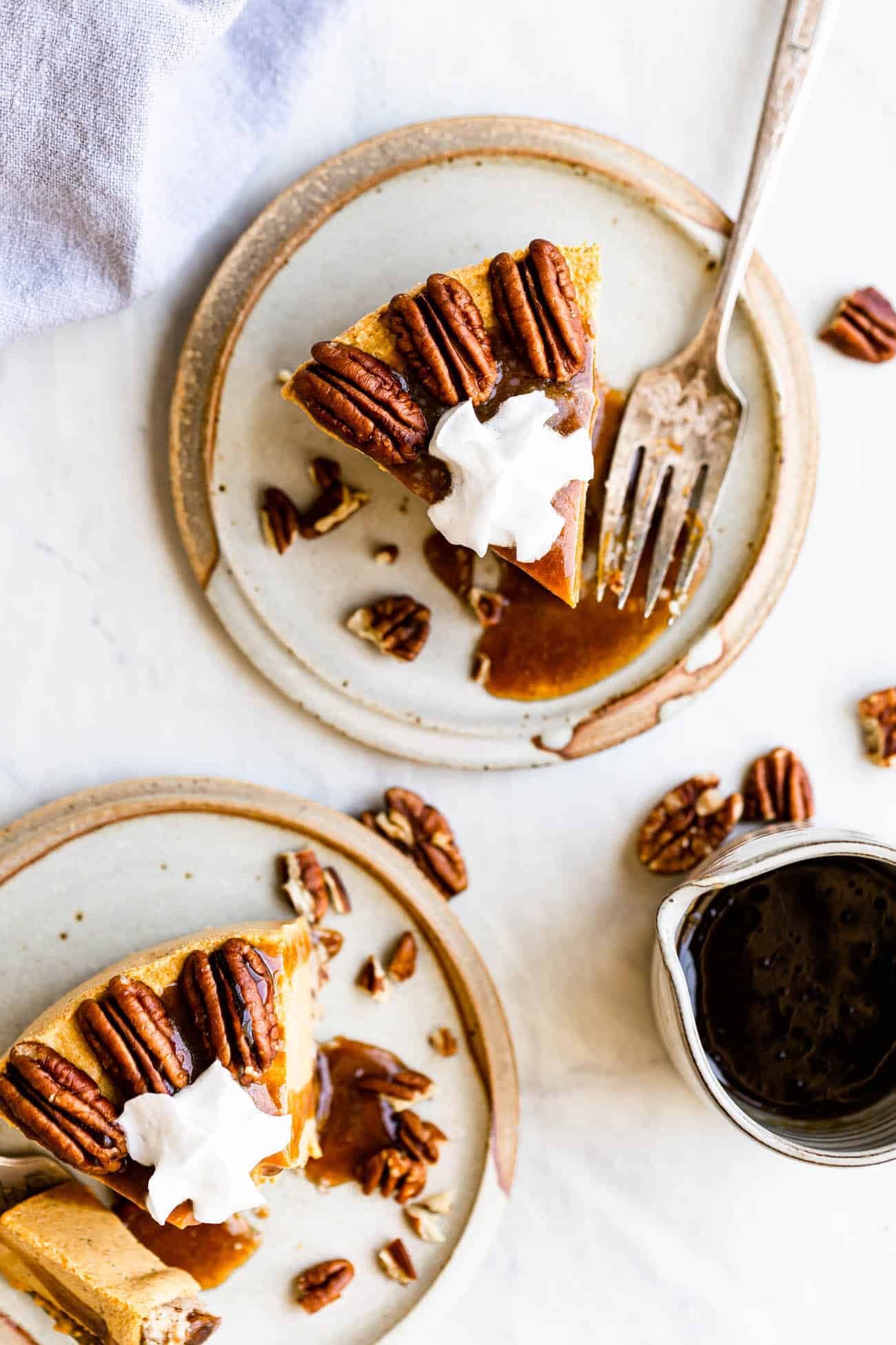 two slices of pumpkin cheesecake on plates with whipped cream and pecans