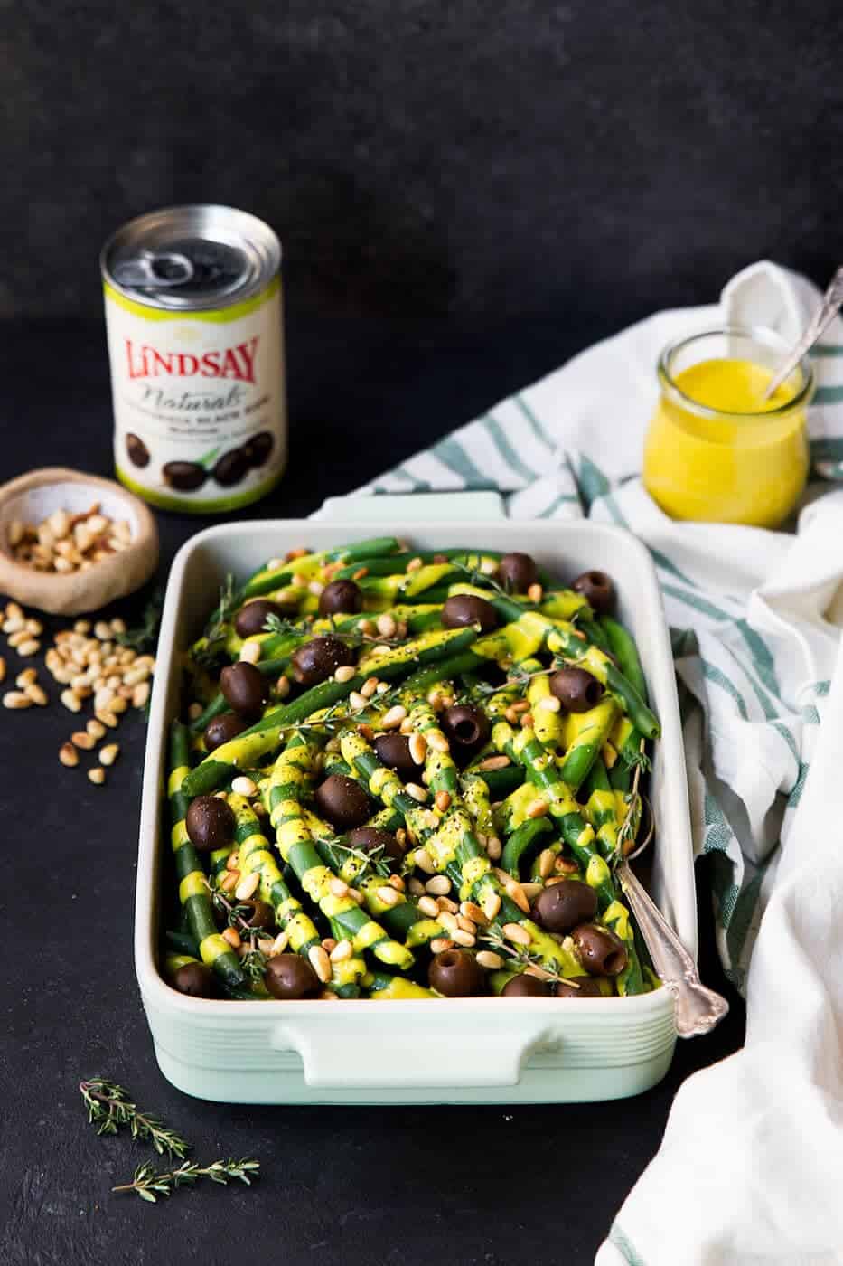 Paleo Green Beans in a serving dish with a can of olive and bowl of nuts