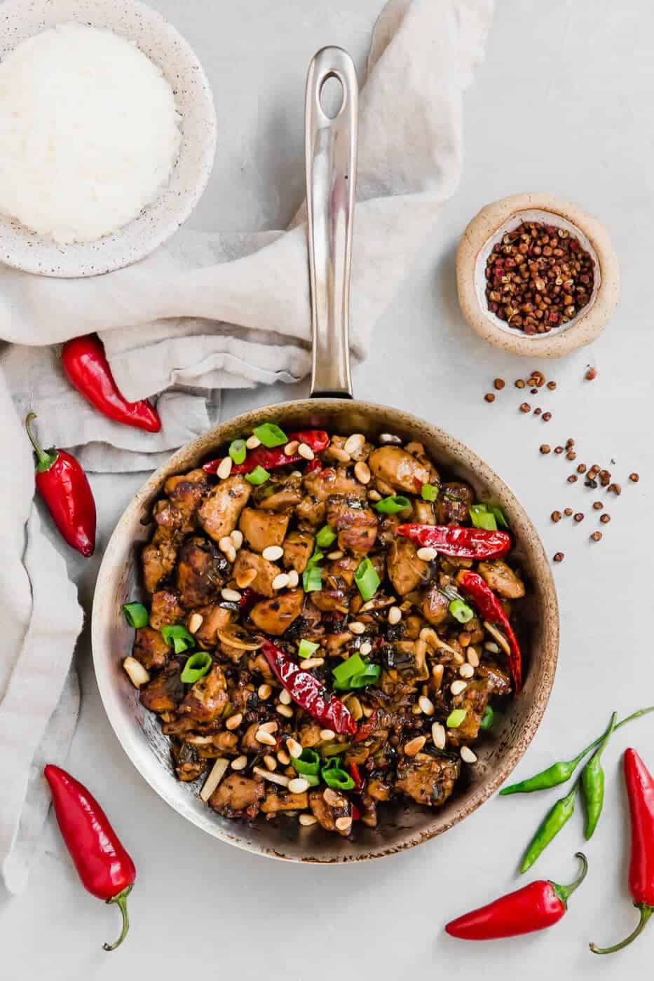 Paleo Kung Pao Chicken in a frying pan with chillies and peppercorns on the side