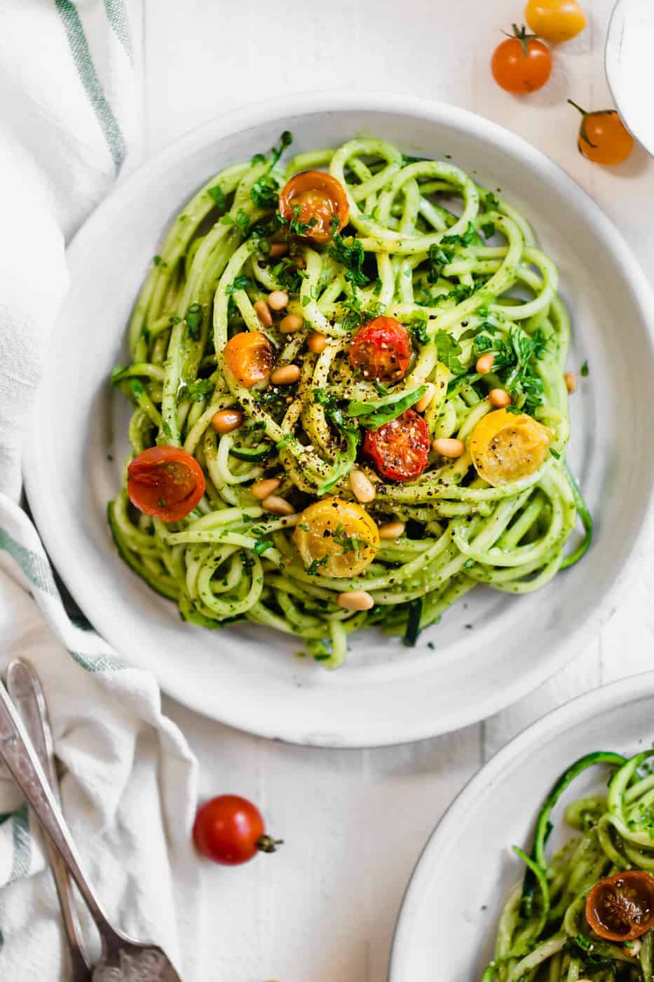 Cooked zucchini noodles with cherry tomatoes and pine nuts in a white bowl