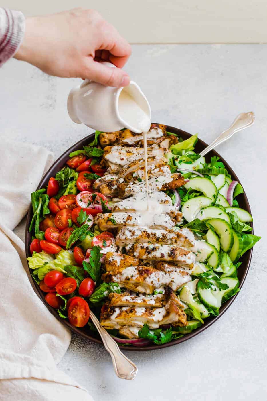 Tahini dressing being poured onto the chicken shawarma salad