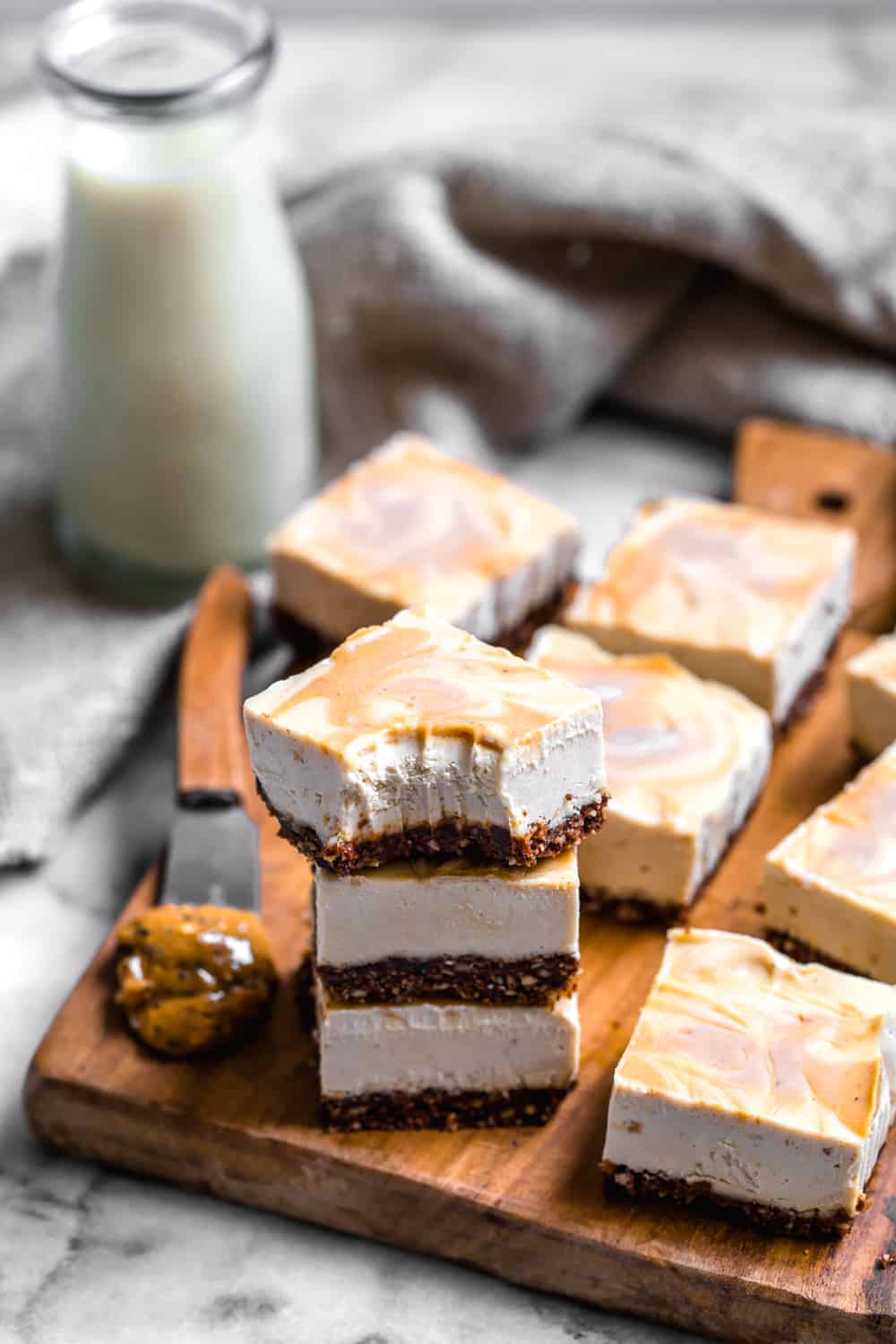vegan peanut butter cheesecake bars with milk in the background on a wooden board