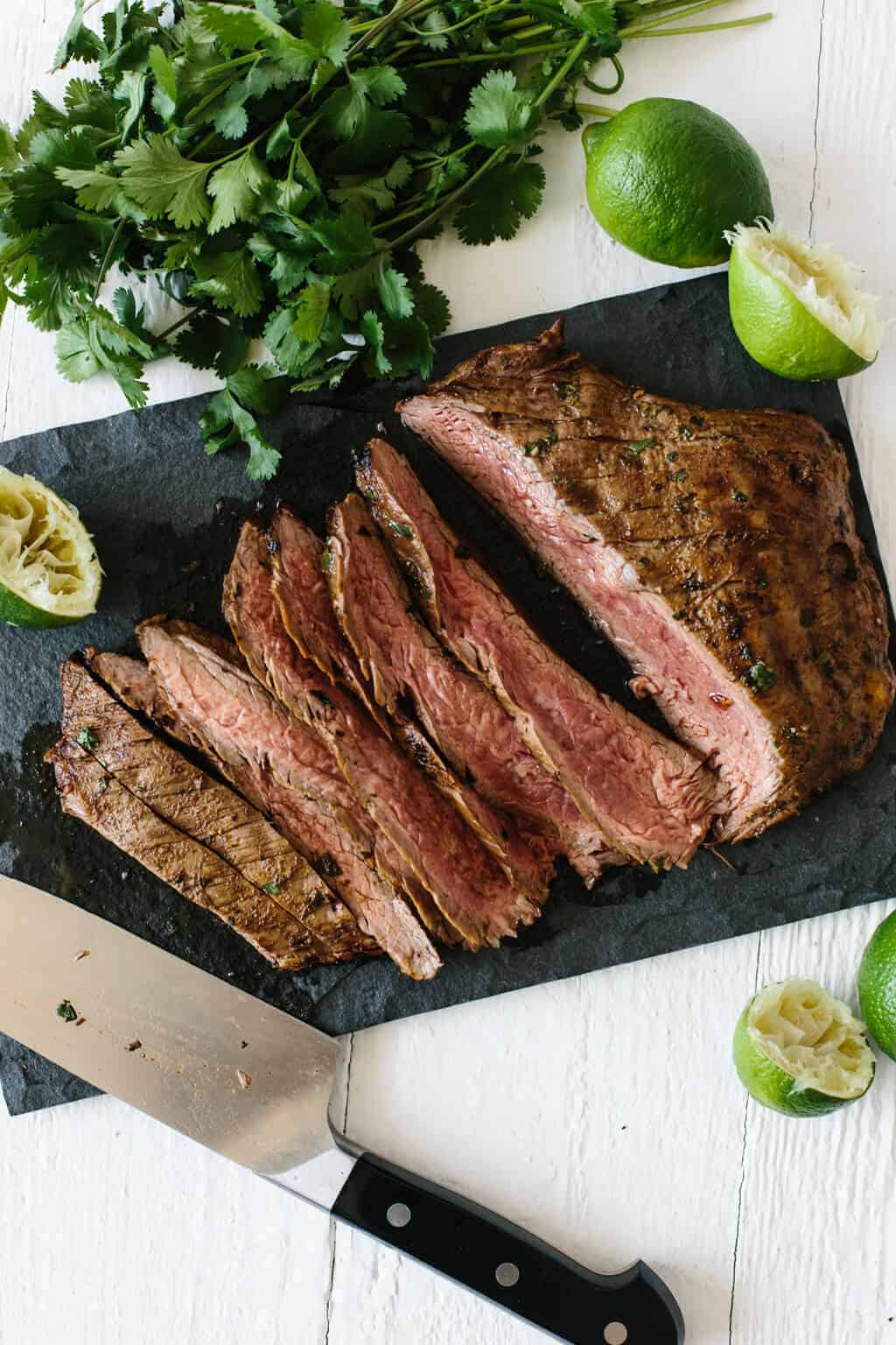 Sliced medium rare steak on a board with lime