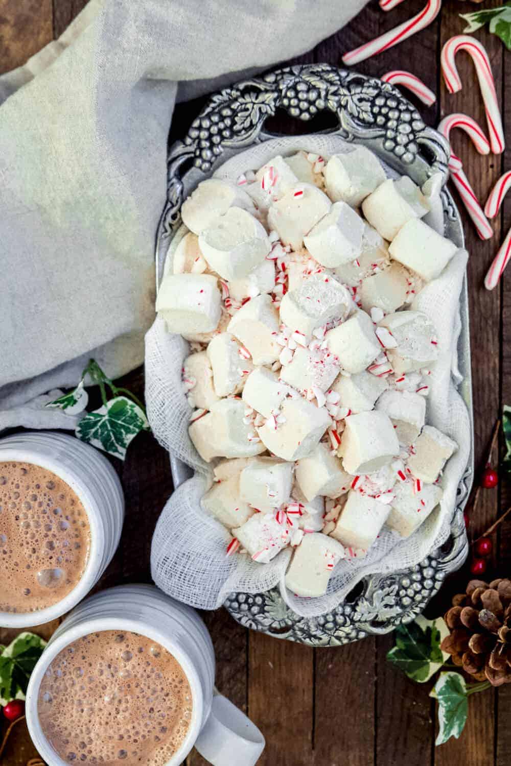 Peppermint marshmallows in a serving dish with two cups of hot chocolate